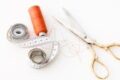 Photo of sewing essentials: scissors, thread, needles, and tape measure on a white background.